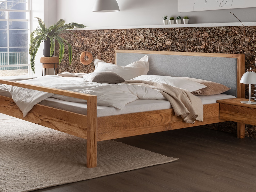 Le lit en bois massif « Capania » séduit par son design épuré, ici avec une tête de lit en feutre et un pied de lit haut